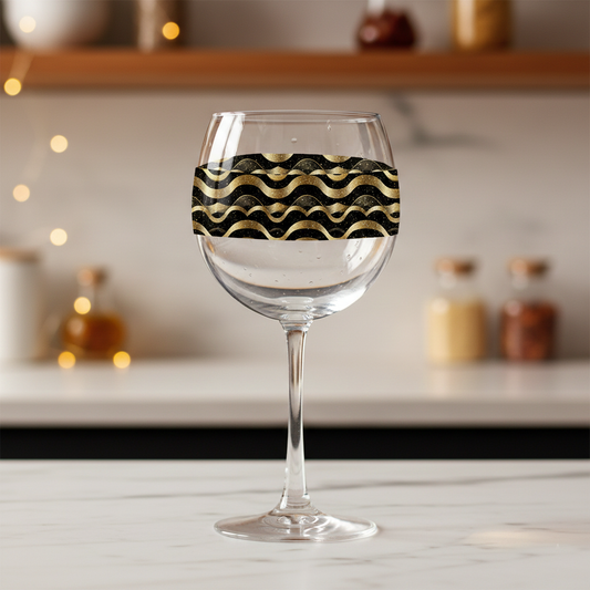 Liquid Gold balloon wine glass with black and gold wavy Art-Deco design on a marnle kitchen counter with blurred background.