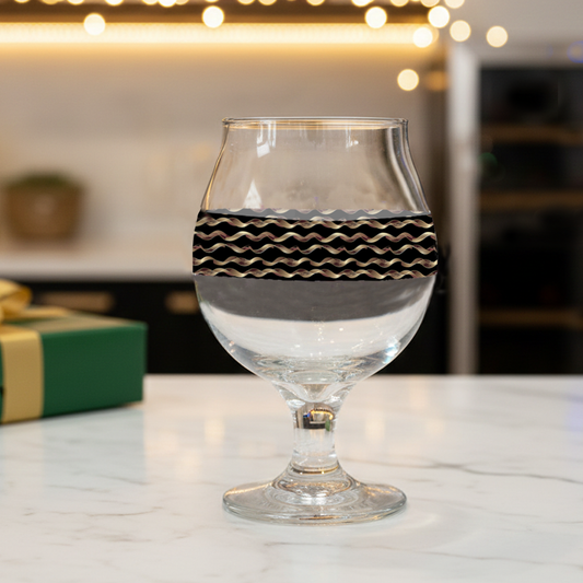 Liquid Gold Belgian beer glass in a black and gold wavy design on a marble surface with blurred background