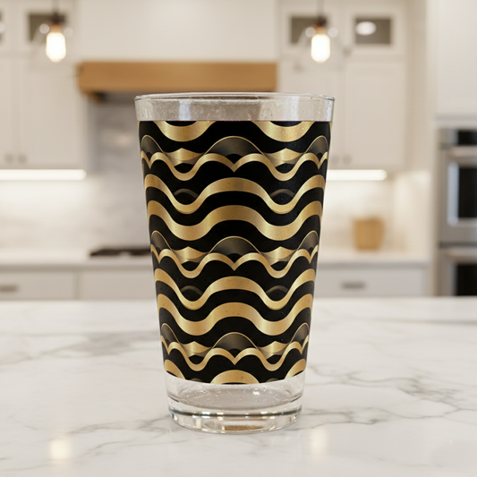 Liquid Gold pint glass with gold and black wavy Art-Deco design on a marble kitchen counter with blurred background.