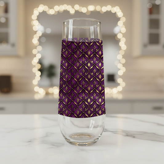 Royal Opulence stemless chmpagne glass with a plum and gold design on a marble surface, blurred lights in the background