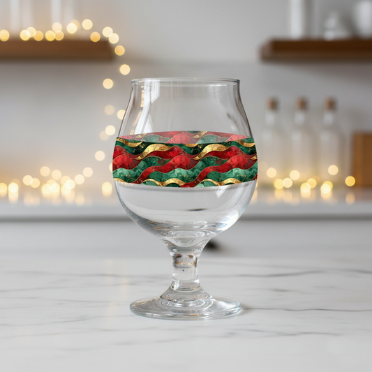Royal Flux Belgian beer glass with red, green, and gold wavy design on a marble surface with blurred lights in the background.
