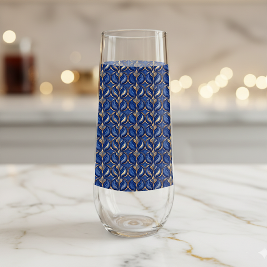 Sapphire Oracle stemless champagne flute glass with navy and gold decorative design on a marble surface with blurred lights in the background