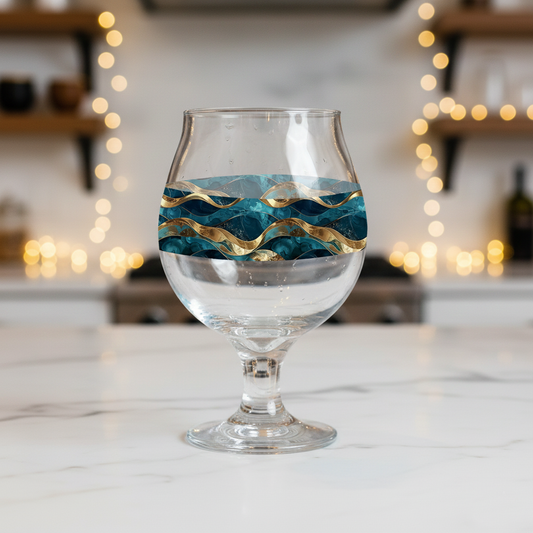 Opulent Teal Belgian beer glass with teal and gold design on a marble counter and blurred kitchen background.