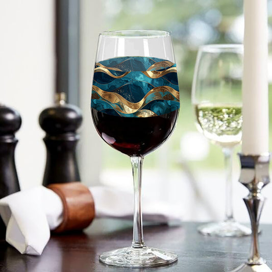 Opulent Teal tall wine glass with red wine highlighting flowing teal and gold wave design and sitting on a table setting with kitchen objects.