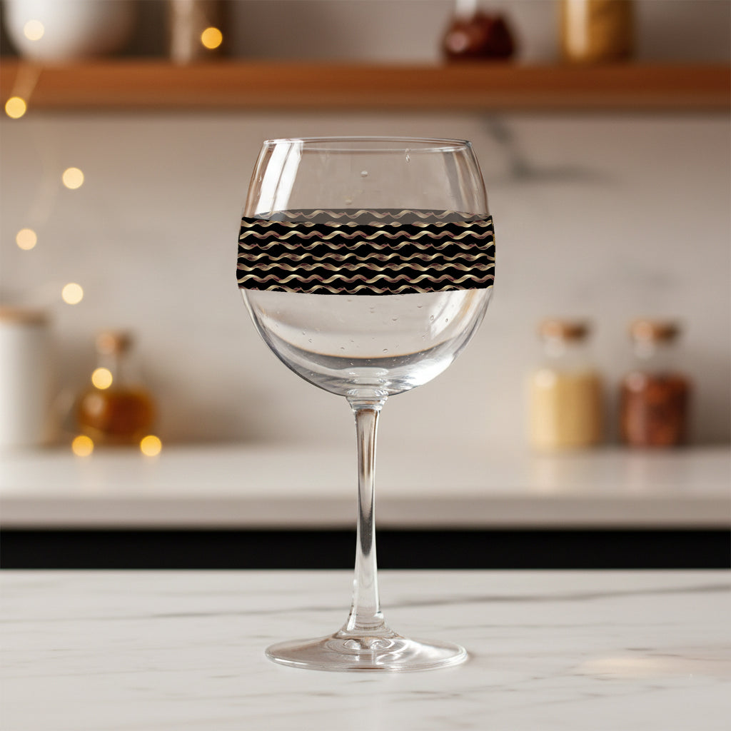 Liquid Gold balloon wine glass with black and gold wavy design on a blurred kitchen background