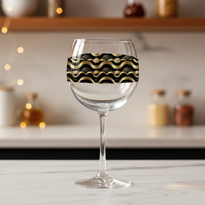 Liquid Gold balloon wine glass with black and gold wavy Art-Deco design on a marnle kitchen counter with blurred background.
