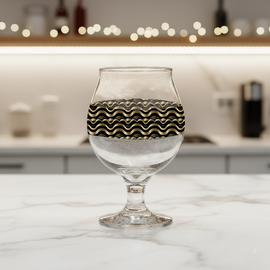 Liquid Gold Belgian beer glass with black and gold closeup on a countertop with blurred lights and background.
