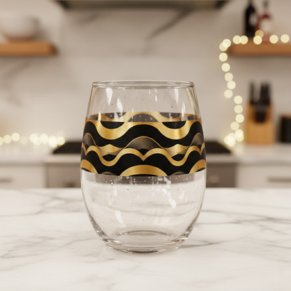 Liquid Gold stemless wine glass with black and gold wavy Art-Deco design on a marble surface with blurred kitchen background.