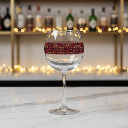 Crimson Jewels balloon wine glass with ruby and gold design on a bar counter with blurred bottles and lights in the background