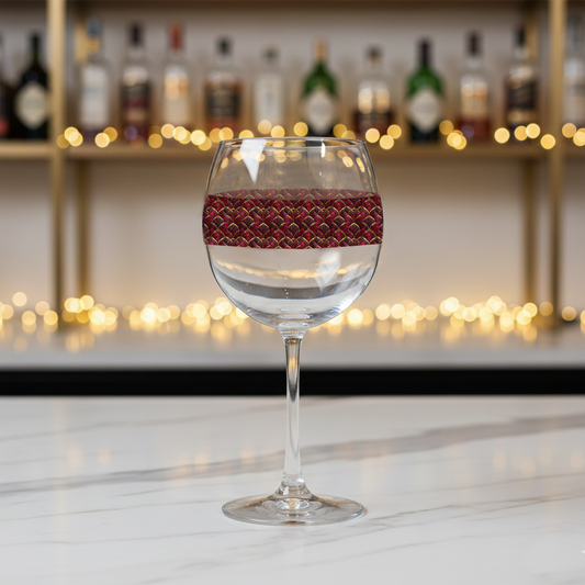 Crimson Jewels balloon wine glass with ruby and gold design on a bar counter with blurred bottles and lights in the background