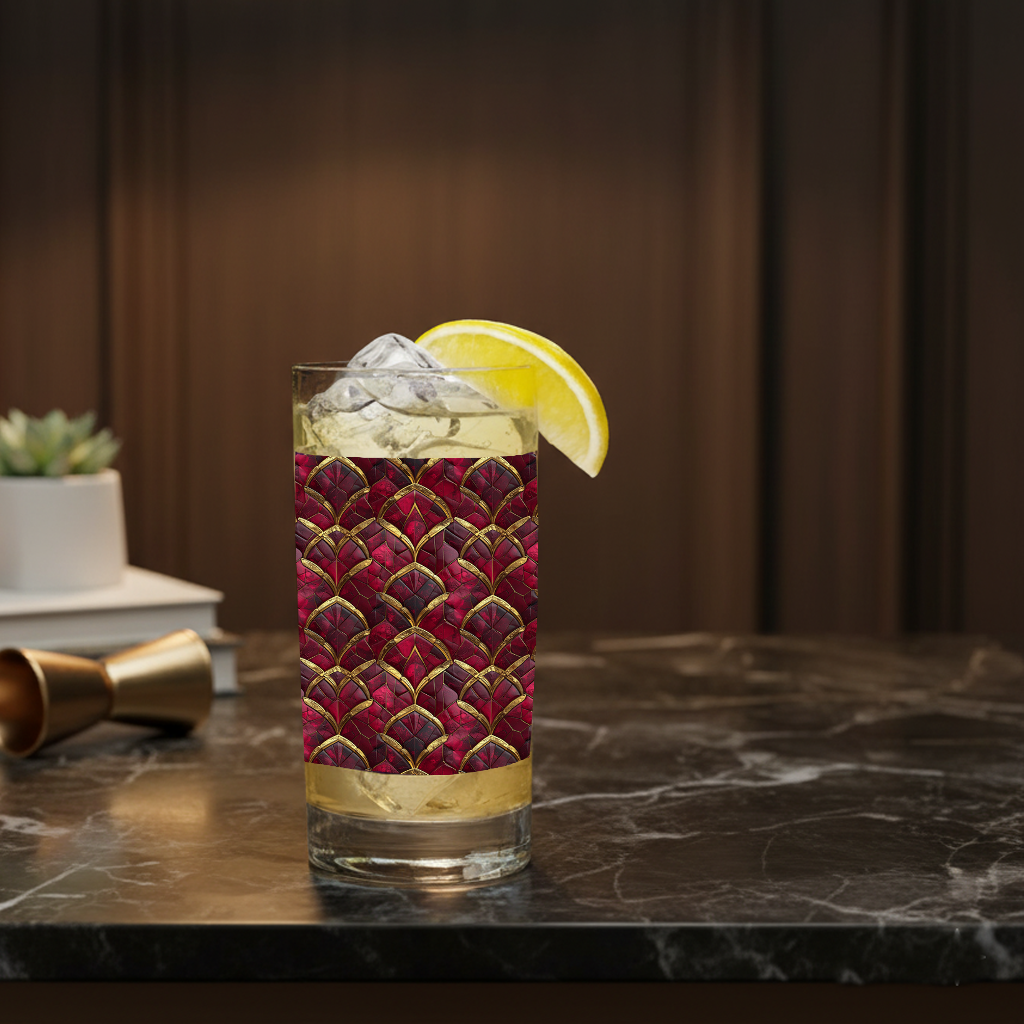 Crimson Jewels highball glass with a ruby and gold design, filled with a cocktail and garnished with a lemon wedge on a dark surface.