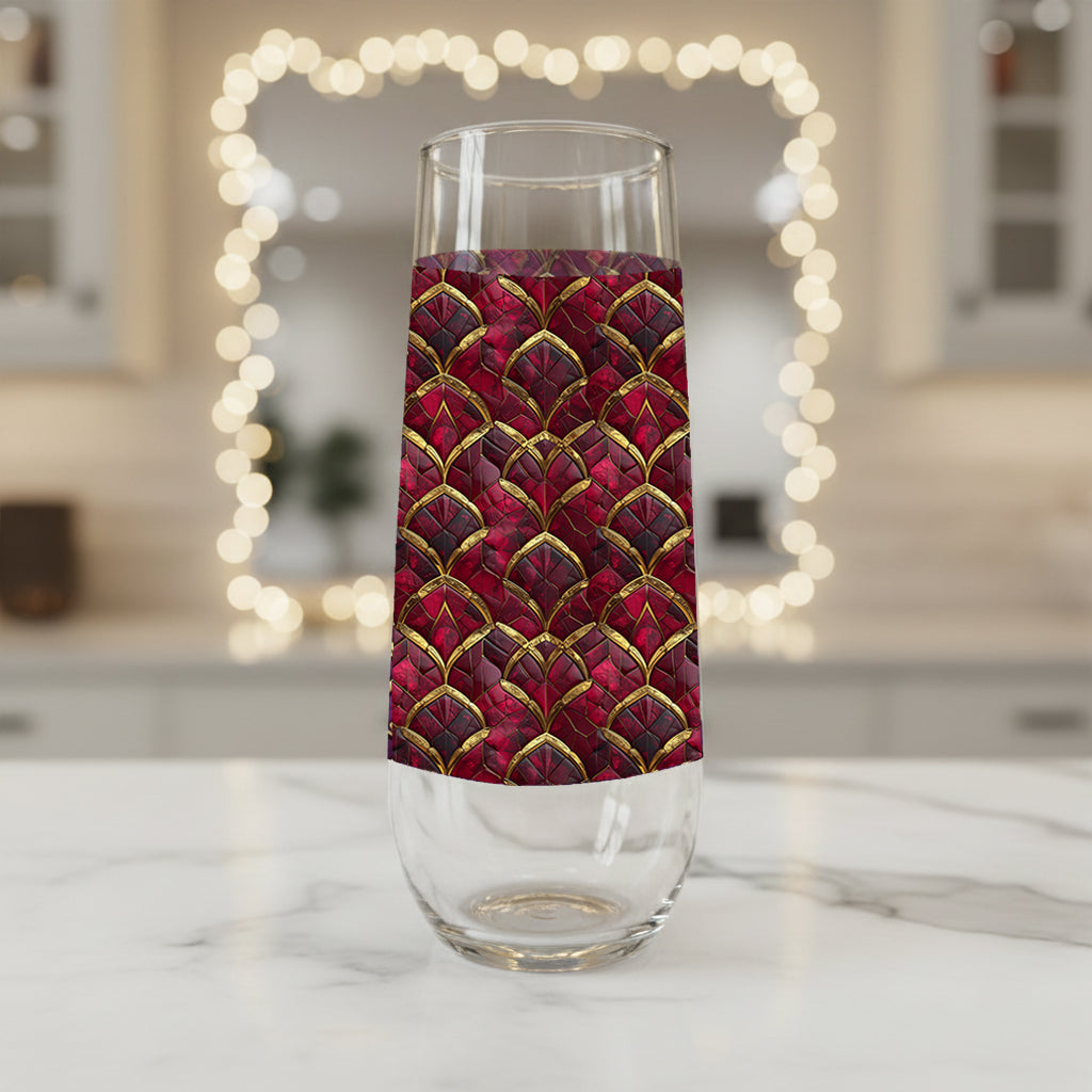 Crimson Jewels stemless champagne glass with a ruby and gold design on a marble surface with blurred lights in the background