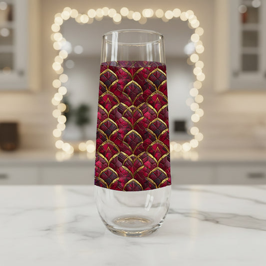 Crimson Jewels stemless champagne glass with a ruby and gold design on a marble surface with blurred lights in the background