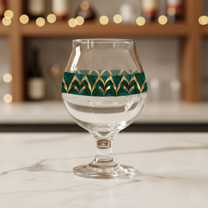 Emerald Royale Belgian clear glass with green and gold decorative design on a marble surface with blurred background