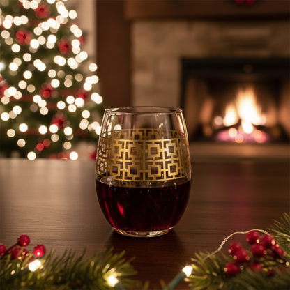 Luxe Gold stemless wine glass filled with red wine with gold geometric design on a table in front of a Christmas tree and fireplace.