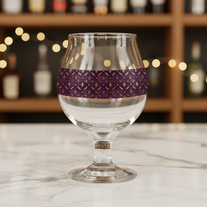 Royal Opulence Belgian beer glass with plum and gold  decorative design on a marble surface with blurred bottles in the background