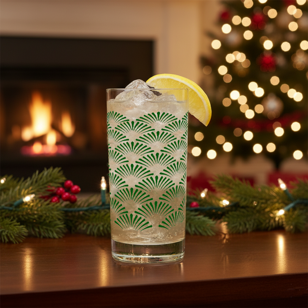 Green Deco highball glass with an Art-Deco design, filled with a cocktail and lemon slice, set against a festive background with a fireplace and Christmas tree.