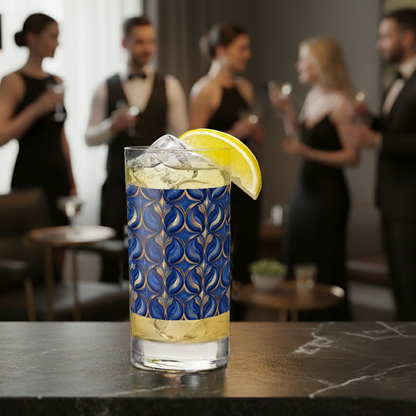 Sapphire Oracle highball glass with cocktail and lemon wedge, with a blue and gold decorative design and a blurred background of people socializing.