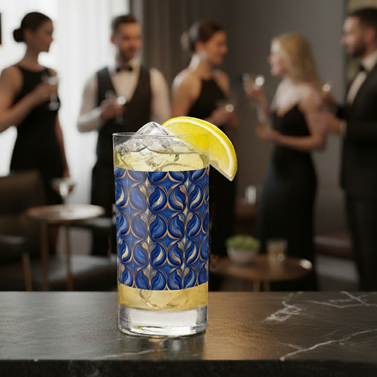 Sapphire Oracle highball glass with cocktail and lemon wedge, with a blue and gold decorative design and a blurred background of people socializing.