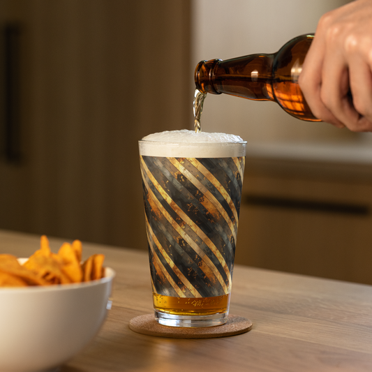 Obsidian Stripes pint glass with black and gold diagonal design, and a hand pouring beer into a glass with a bowl of chips on a wooden table.