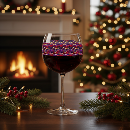 Fluid Marble balloon wine glass filled with red wine and a purple and gold design on a table with pine branches and berries, with a lit Christmas tree and fireplace in the background.