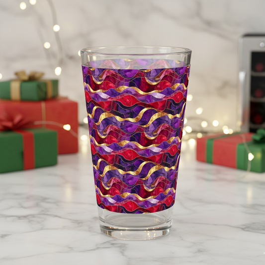 Fluid Marble pint glass in a purple and gold pattern on a marble surface with blurred holiday gift boxes in the background.