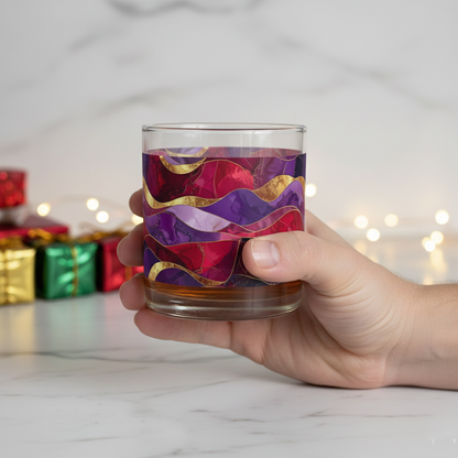 Hand holding the Fluid Marble signature rocks glass with purple and gold pattern  on a marble countertop.