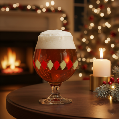 Ruby and Gold Belgian glass filled with  beer and a colorful diamond design on a table in front of a Christmas tree and fireplace.