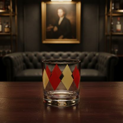 Ruby and Gold rocks glass with Art-Deco harlequin design on a wooden table in a room with a couch and framed portrait.