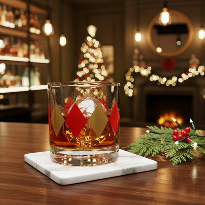 Ruby and Gold rocks glass of whiskey in bold  harlequin design on a coaster with Christmas decorations and a fireplace in the background