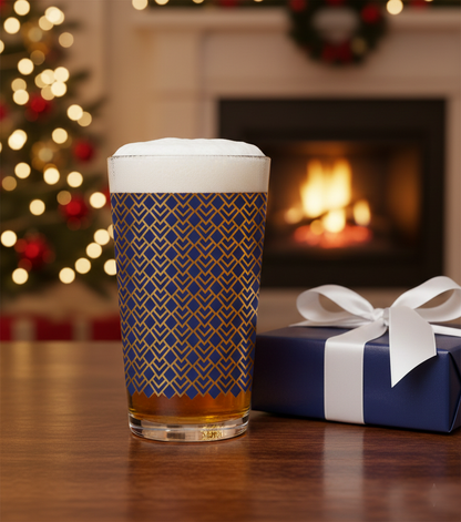 Sapphire Deco pint glass with Art-Deco design and filled with beer. Sitting on a table next to wrapped gift and Christmas tree and fireplace in the background.