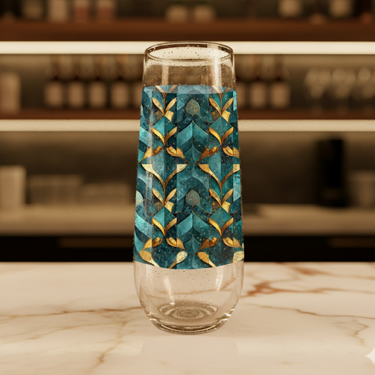 Gilded Patina stemless champagne flute glass with teal and gold geometric pattern on a marble surface with blurred background